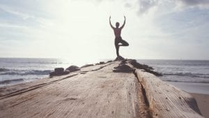 une silhouette se tient face à la mer en effectuant une position de yoga