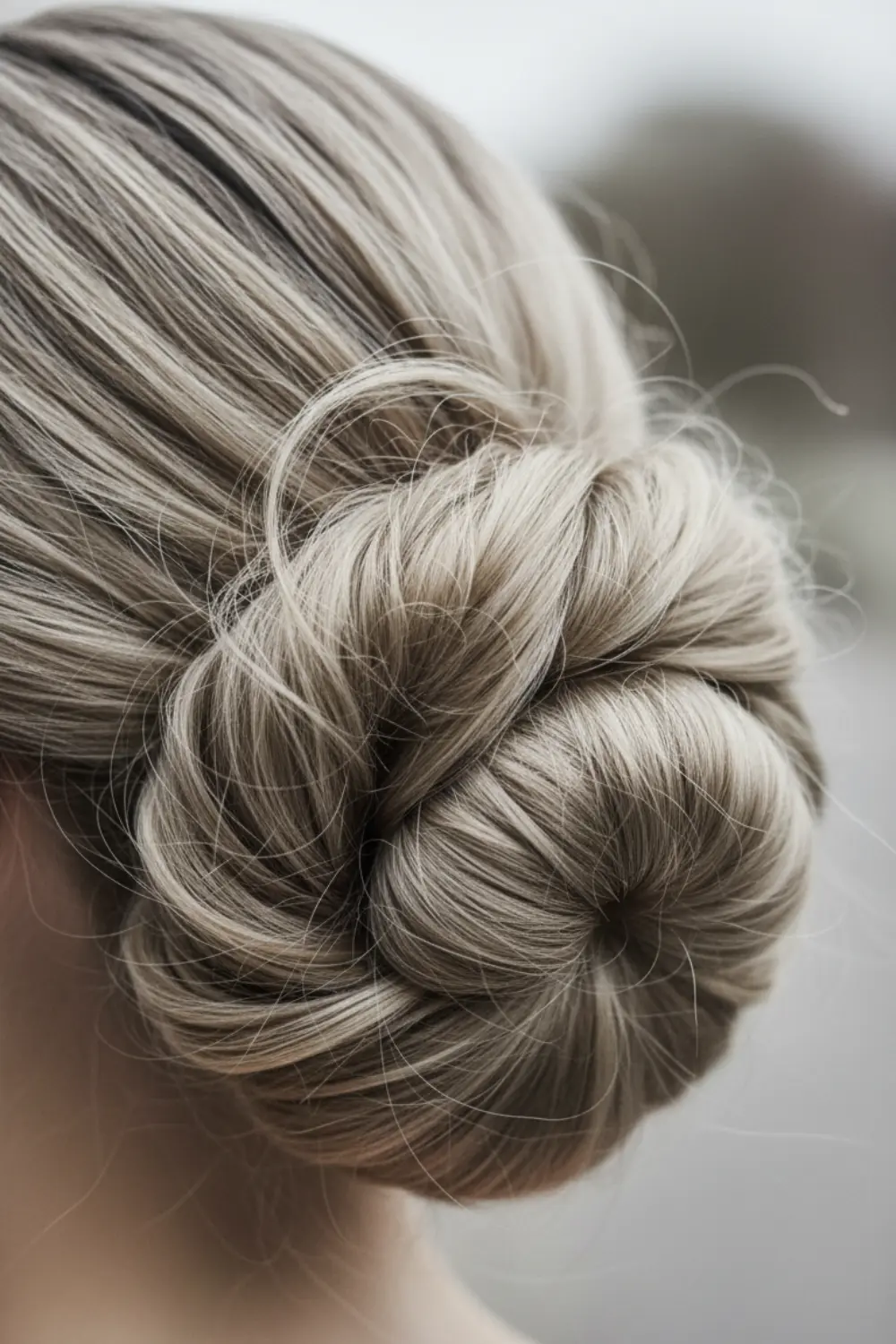Gros plan sur un chignon cachemire texturé et flou aux tons beige chaud et gris perle, traité comme une sculpture capillaire délicate.