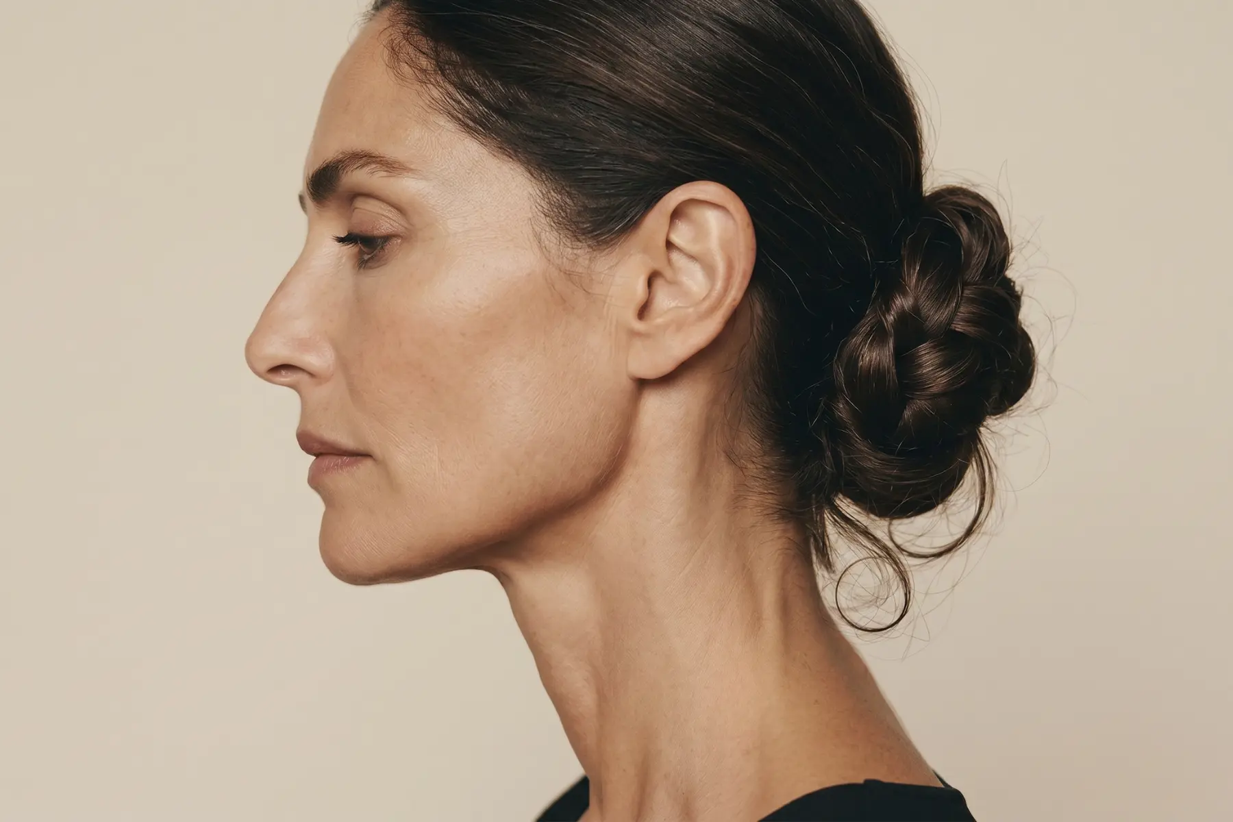 Femme de 45 ans de profil, chignon bas flou sur nuque dégagée, coiffure d'été élégante et naturelle, lumière douce.