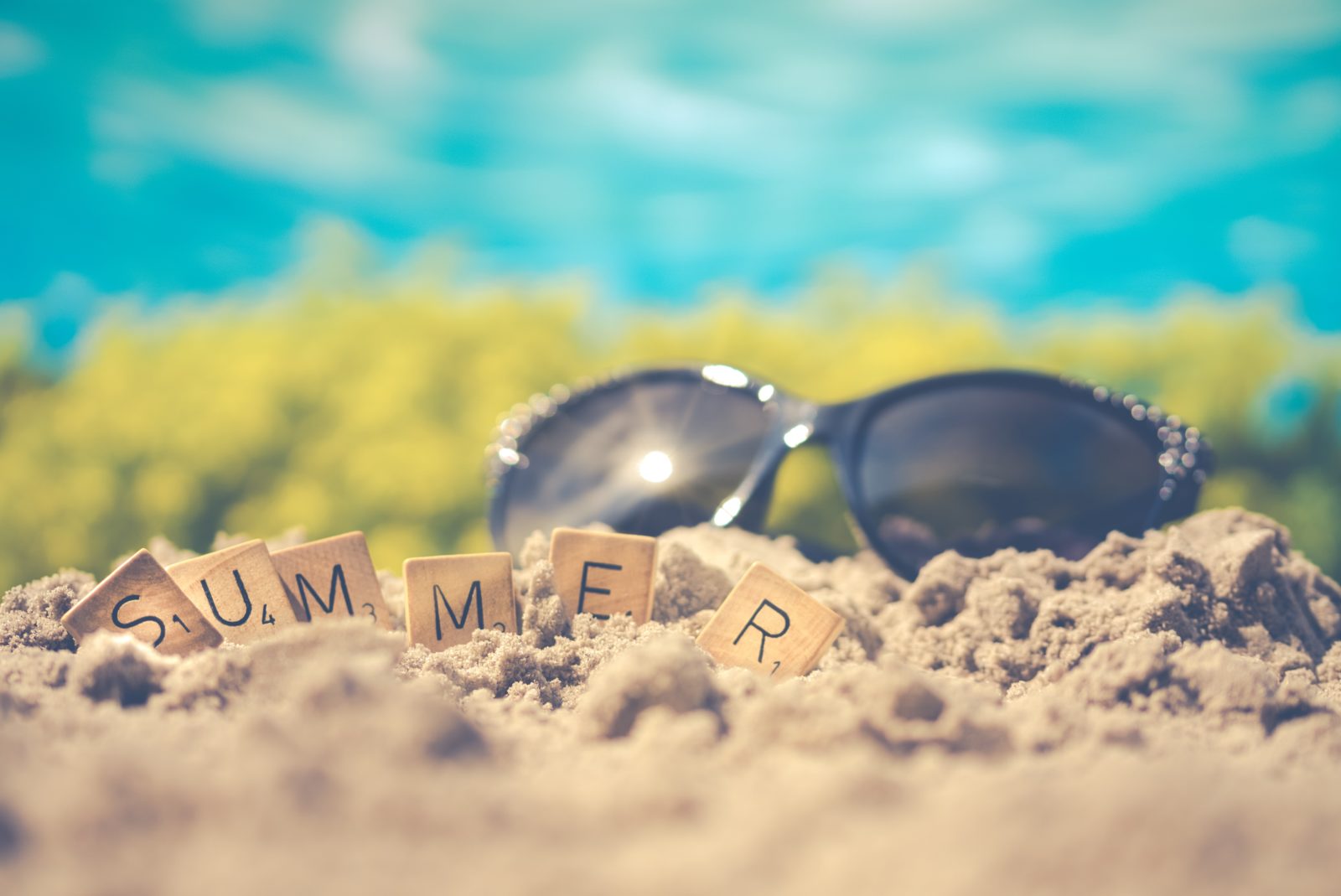 Lunettes de soleil et lettres formants le mot Summer dans le sable.