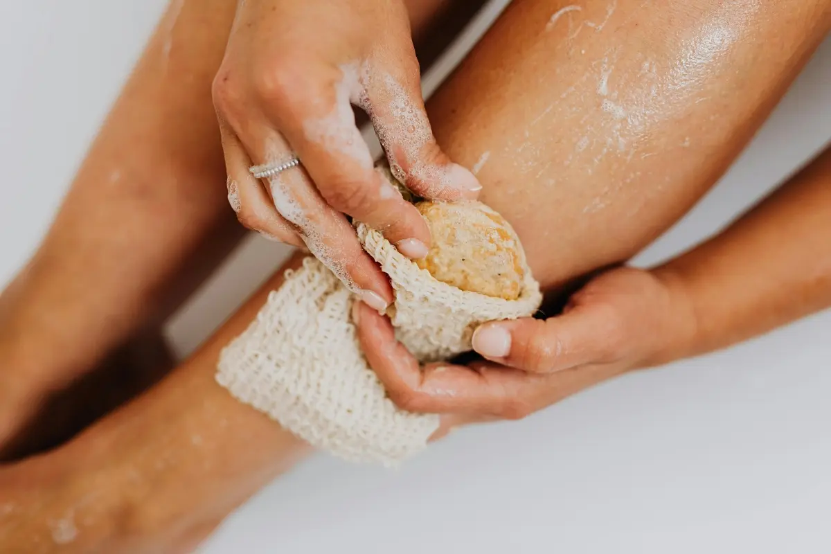 Mains utilisant un pain de savon exfoliant dans un filet de sisal sur la jambe
