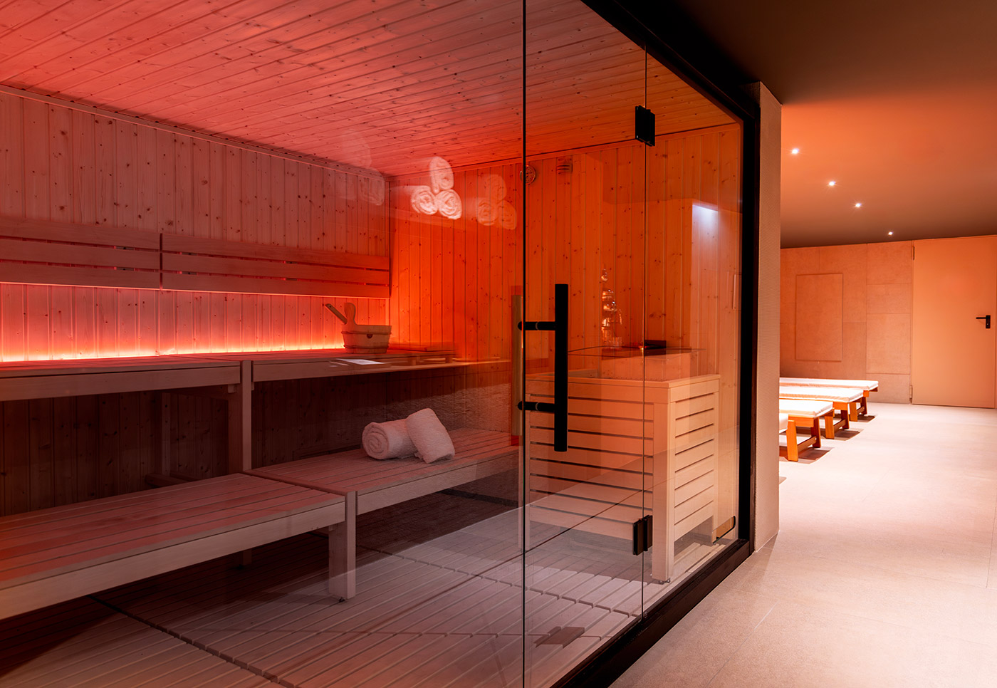 Sauna moderne en bois avec éclairage tamisé rouge et serviettes pliées.