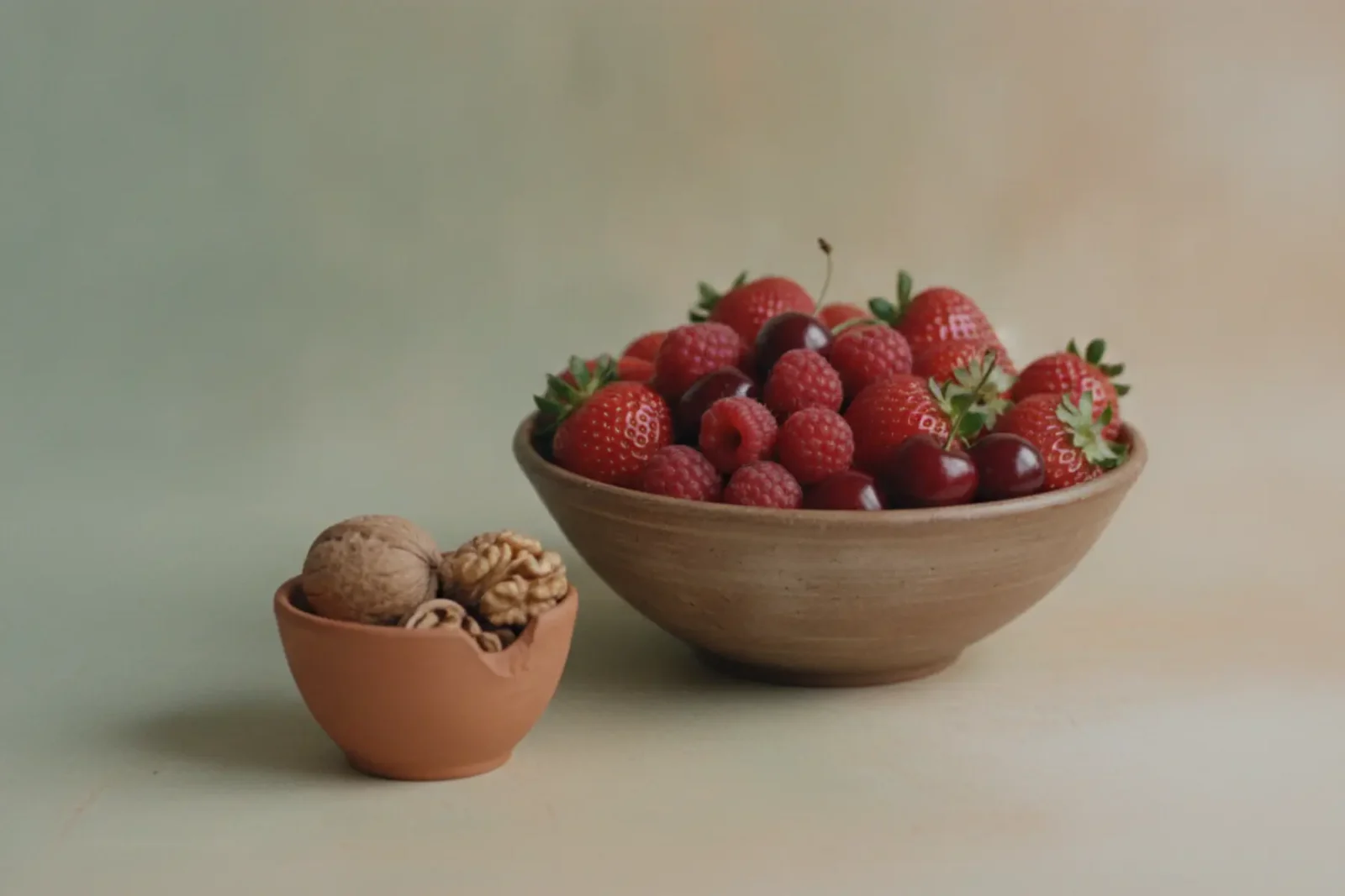 Nature morte épurée d'un bol de fruits rouges et d'une coupelle de noix.