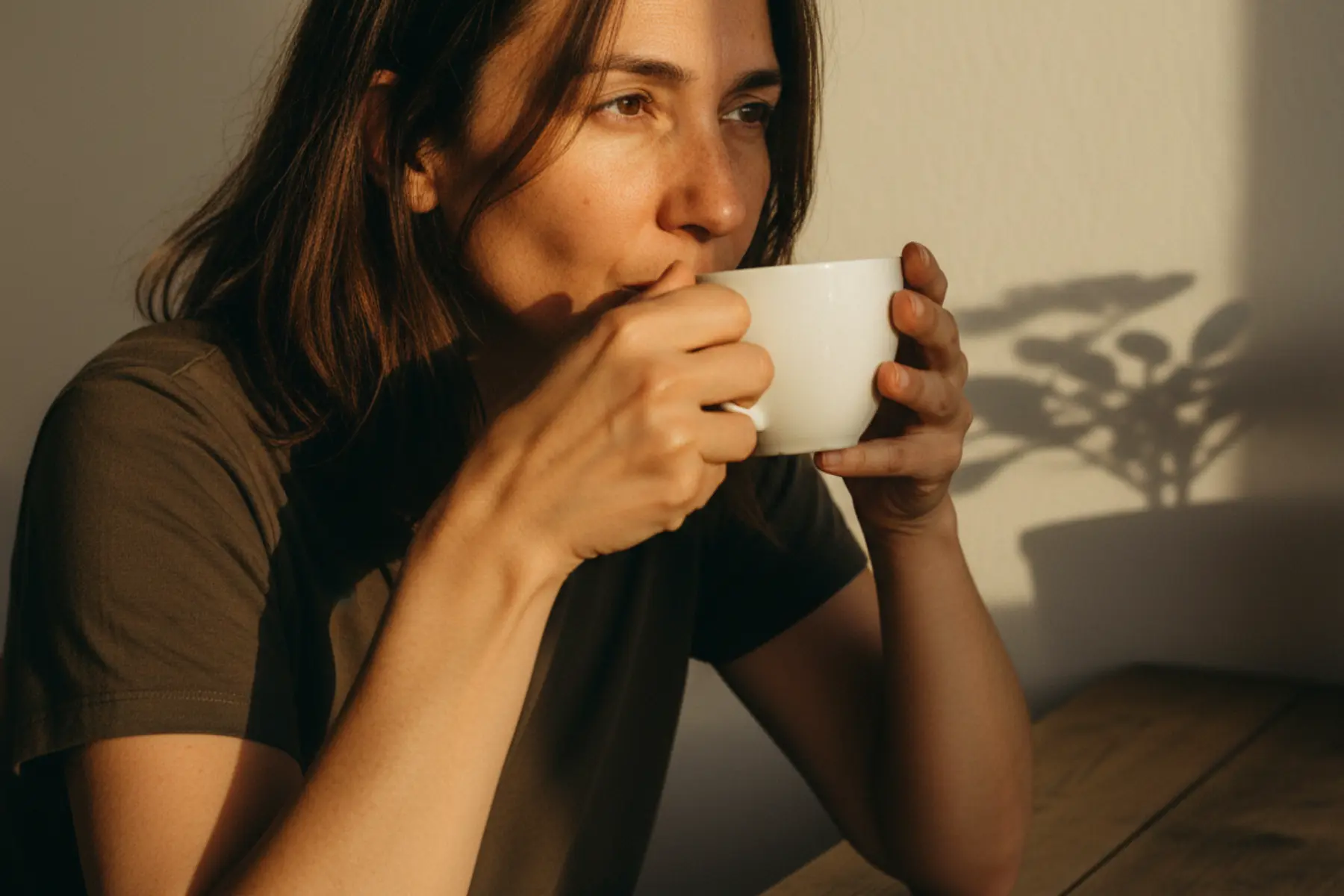Les bienfaits de la naturopathie après 40 ans pour rester en pleine forme 1 Femme d’une quarantaine d’années assise à une table, une tasse à la main, lumière naturelle rasante, peau réelle sans retouche
