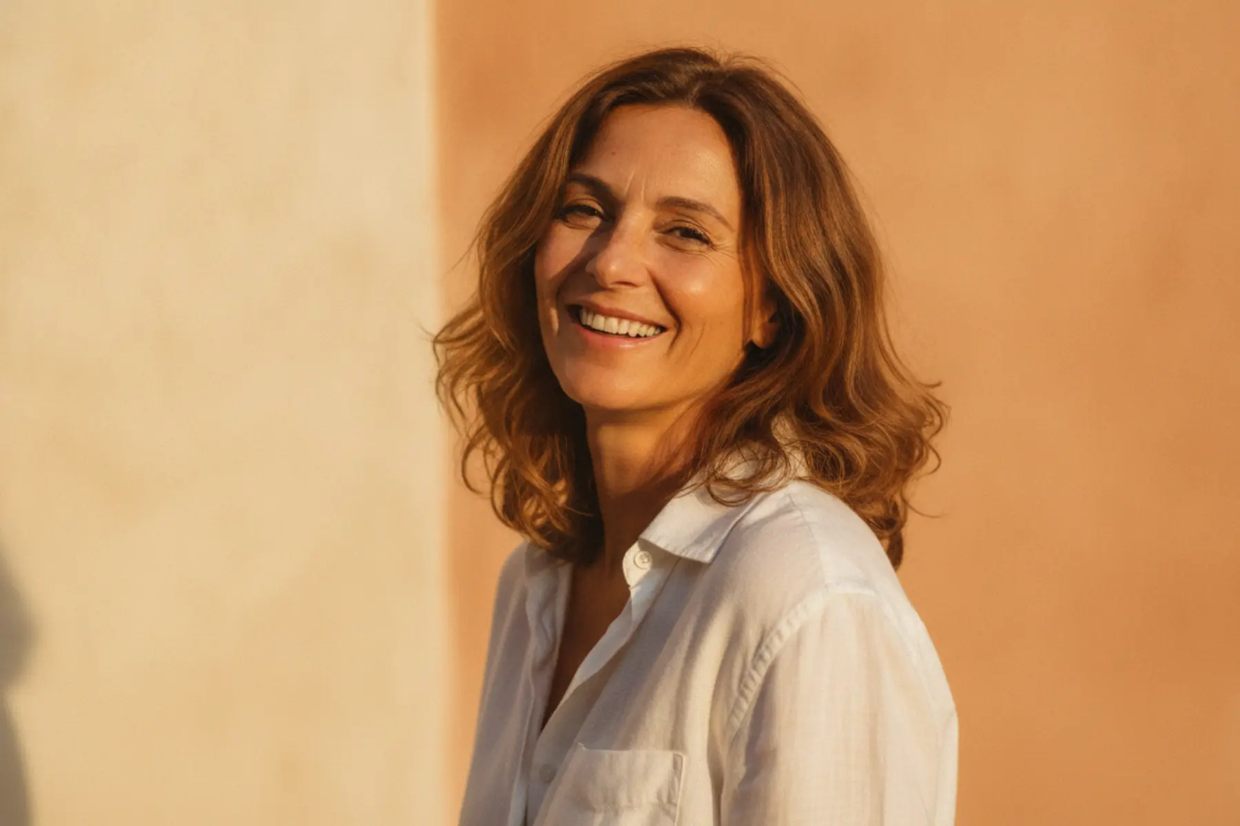 Femme d’une cinquantaine d’années sourire serein visage lumineux fond chaud renouvellement cellulaire peau mature