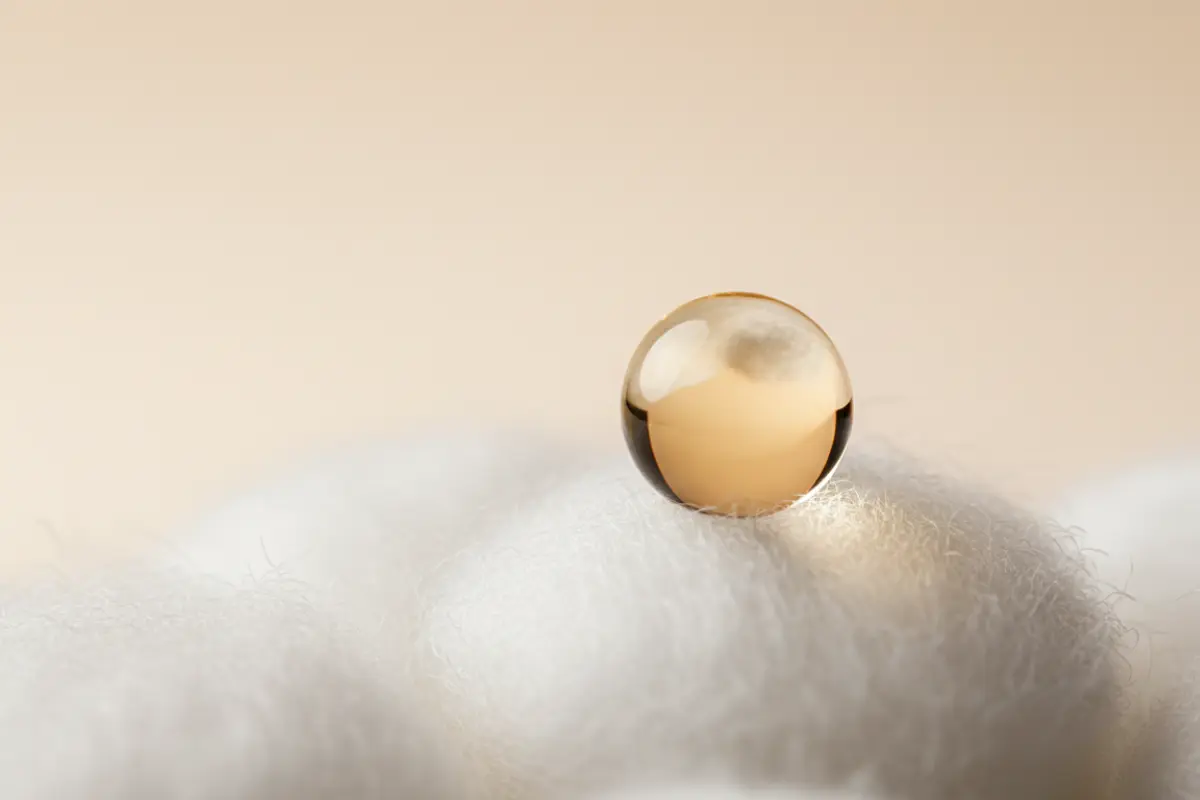 Les bienfaits de l’huile de ricin pour une peau mature et un regard reposé 2 Goutte d’huile de ricin sur un coton, fond beige clair, macro détail texture