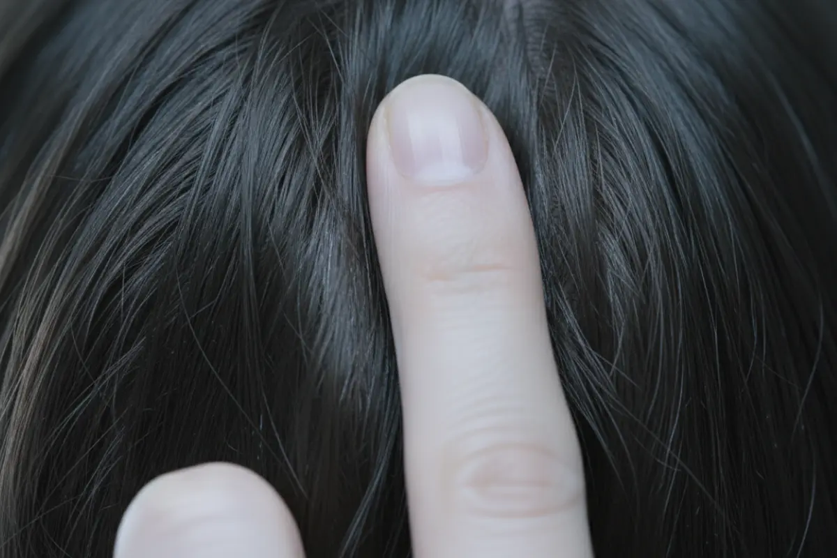 Sublimer la densité de vos cheveux après quarante ans 4 Macro d’un cuir chevelu hydraté avec un doigt effectuant un massage circulaire doux, lumière froide de studio.
