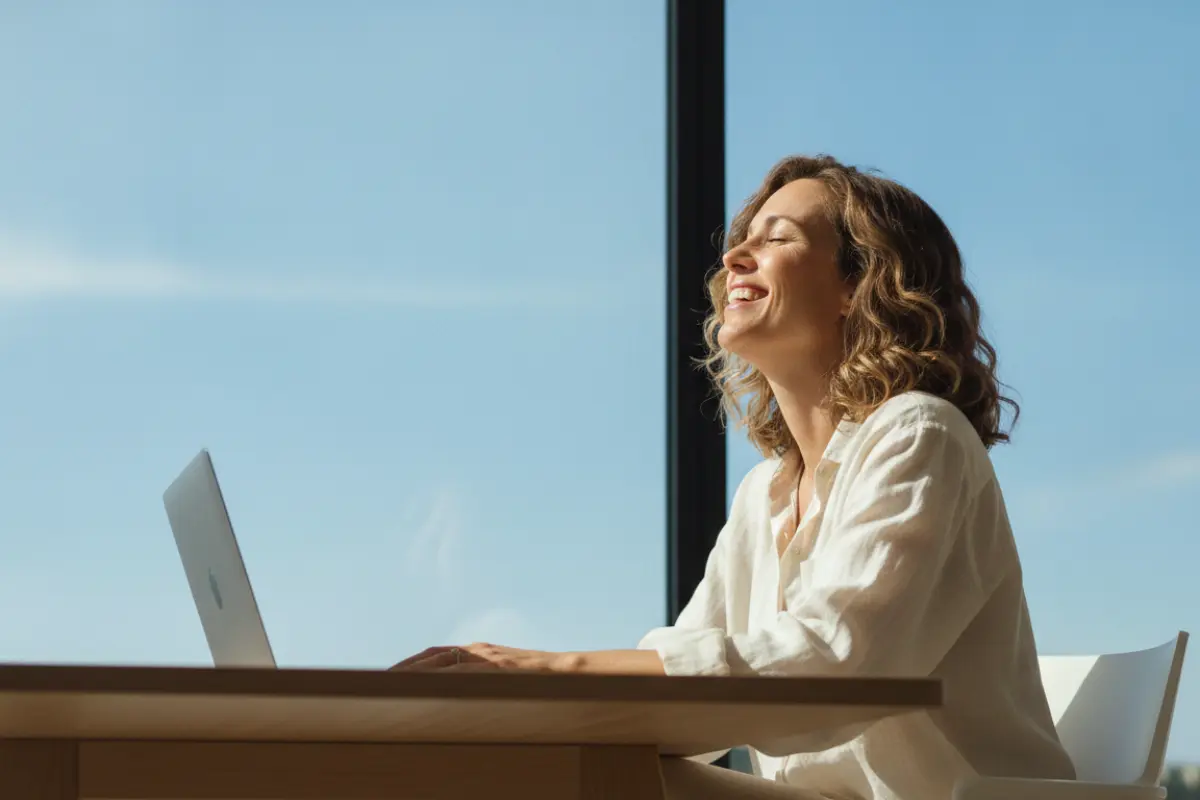 Femme souriante au bureau regardant au loin par la fenêtre pendant une pause du yoga des yeux.