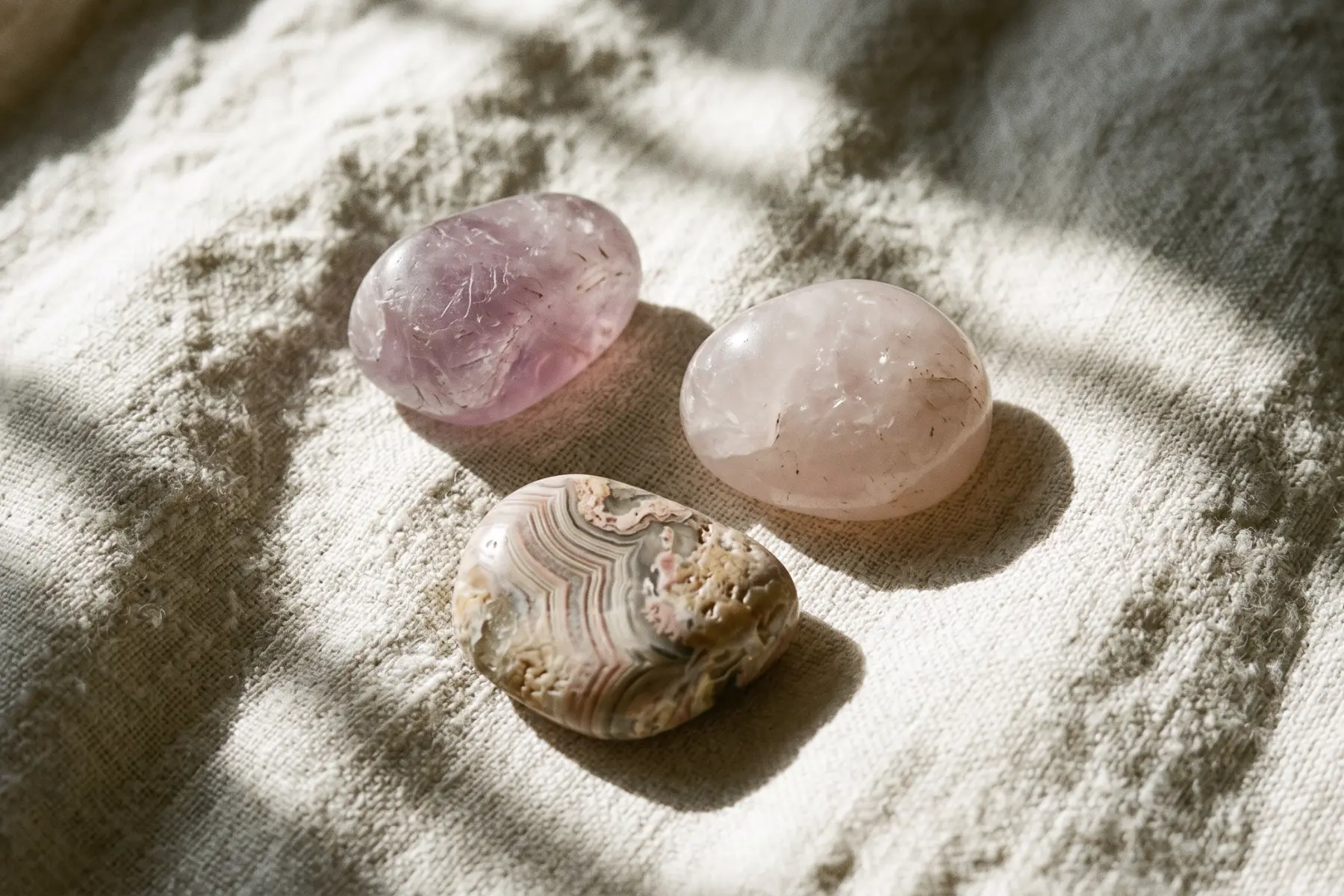 Pierres roulées de lithothérapie disposées sur un linge blanc : améthyste, quartz rose et agate du Botswana