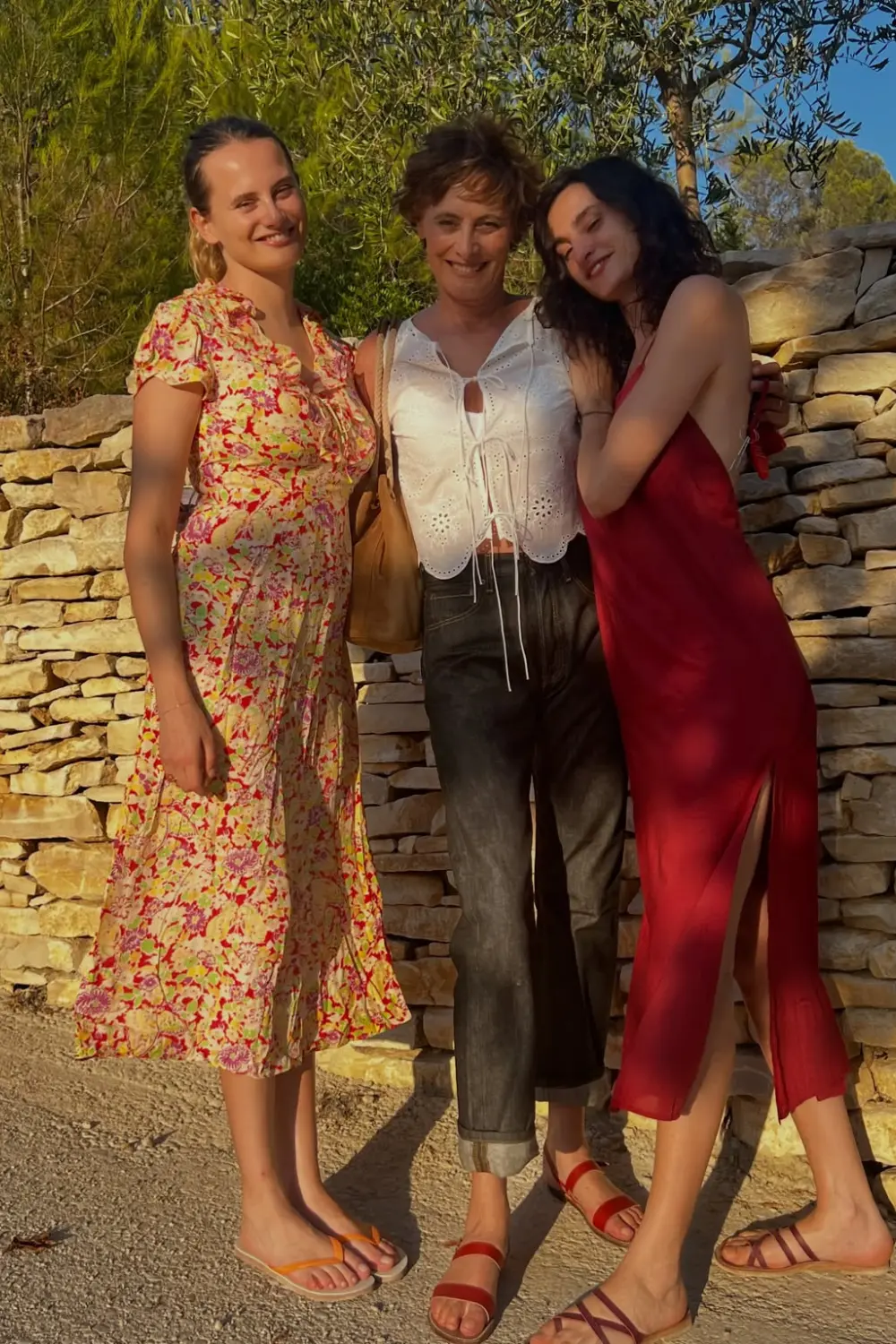 Inès de la Fressange avec ses 2 filles nine et Violette, complices posant devant un mur en pierres sèches dans des tenues d'été élégantes