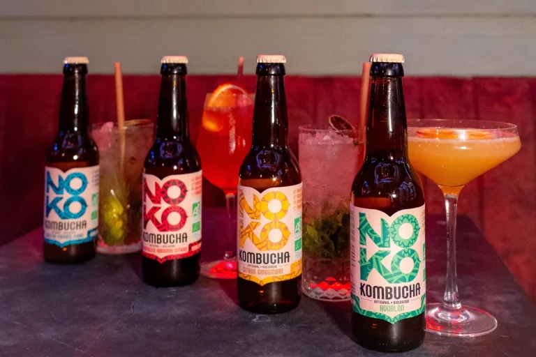 Assortiment de bouteilles de kombucha bio Noko et de verres de cocktails sur une table de bar.