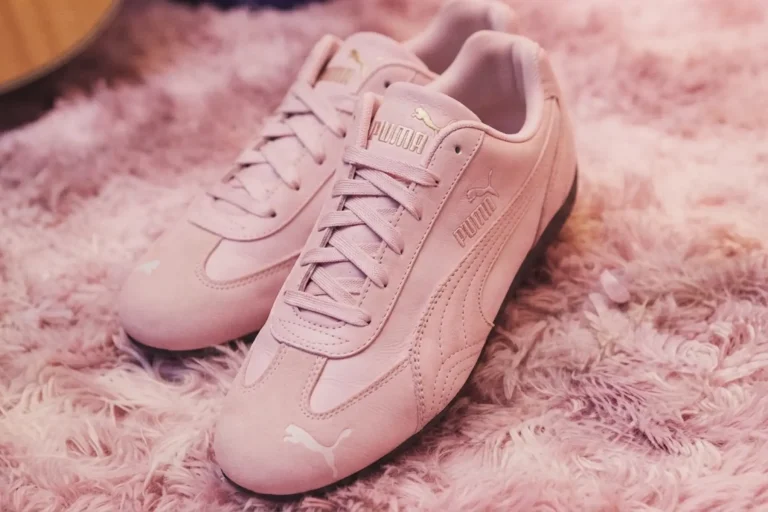 Gros plan sur les baskets Puma Speedcat rose poudré aux détails dorés sur un tapis moelleux rose.
