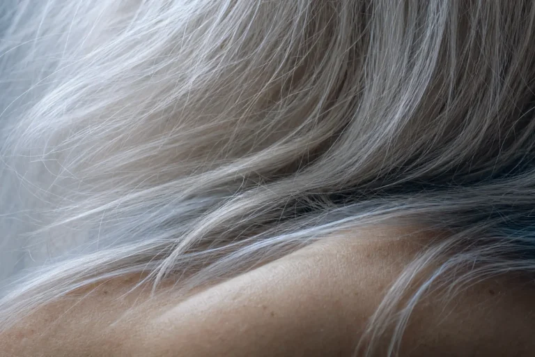 Going grey : comment accepter ses cheveux blancs avec assurance et élégance 1 Gros plan macro de cheveux blancs argentés baignés d'une lumière naturelle froide, texture et mouvement authentiques.