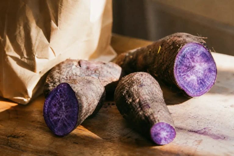 Bien-être : quel est ce superaliment pourpre et sans caféine qui détrône le matcha ? 8 Tubercules d'ube frais coupés dévoilant une chair violette intense posés à côté d'un sachet kraft sur une table en bois, lumière naturelle