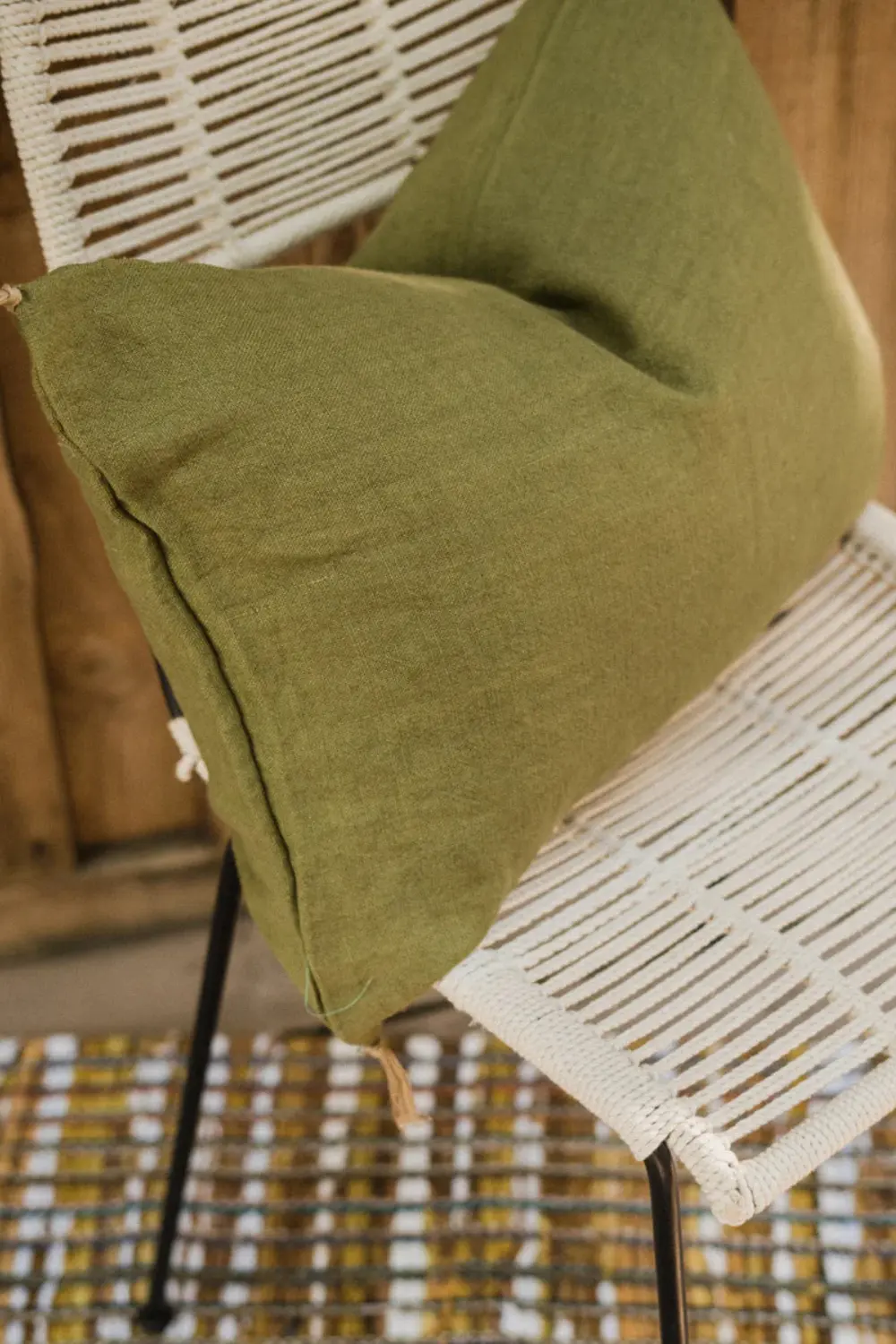 Housse de coussin en lin vert olive Luni par Caravane posée sur une chaise tressée.