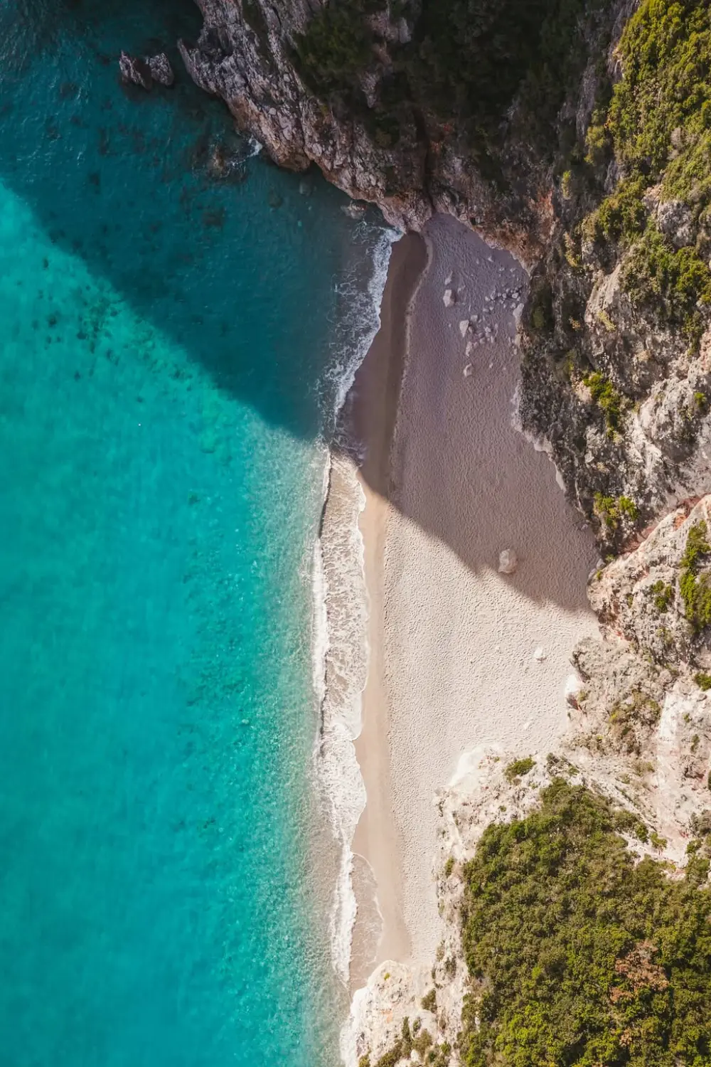Vue aérienne verticale de la plage de Gjipe bordée de falaises et d'une mer turquoise.