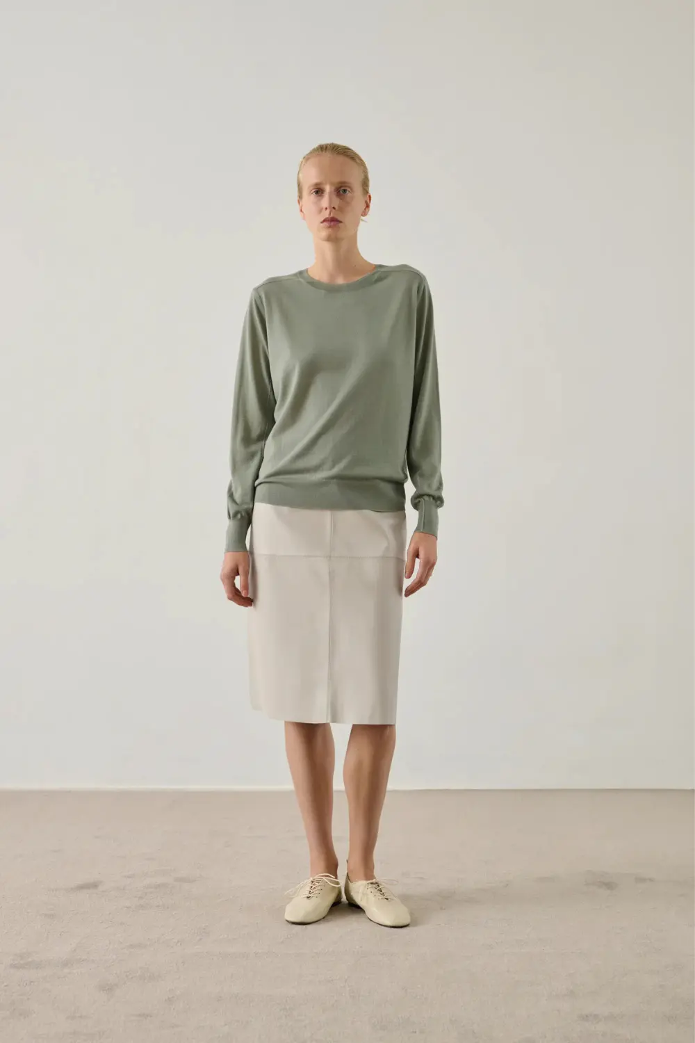 Rentrée 2026 : les 5 pièces d'allure qui font pivoter tout le dressing 4 Mannequin portant un pull en laine mérinos vert sauge Soeur avec une jupe beige droit.