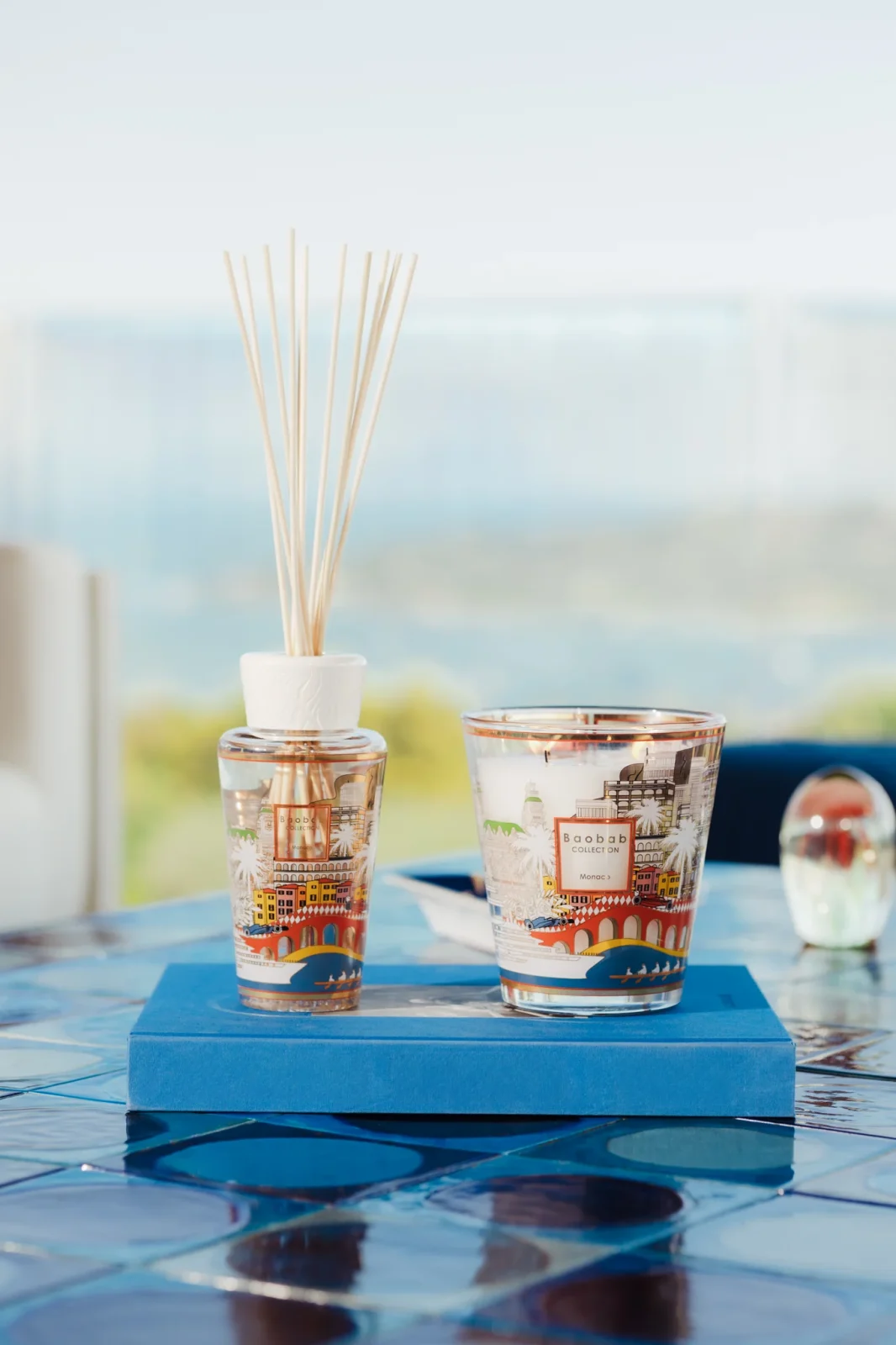 Duo bougie et diffuseur Monaco Baobab Collection, exclusivité Segraeti Monte-Carlo, sur une table en céramique bleue.